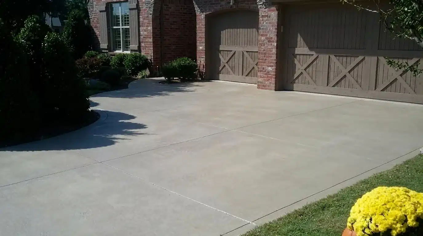 Stained concrete driveway in soft natural sandstone color leading to a brick home with carriage-style garage doors